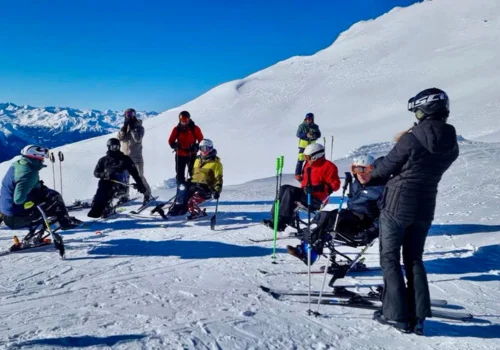Skiferieforalle/Sustravel.dk folk, nogle i kørestol, på toppen af et bjerg i ski udstyr, der holder pause.